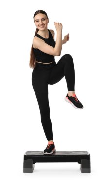 Beyaz arka planda adım platformuyla aerobik egzersiz yapan genç bir kadın.