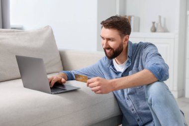 Çevrimiçi bankacılık. Kredi kartı ve dizüstü bilgisayarı olan mutlu genç adam evde ödeme yapıyor.