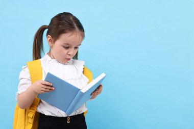 Sırt çantalı, açık mavi arka planda kitap okuyan sevimli küçük bir kız. Metin için boşluk