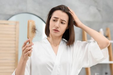 Banyoda saçı dökülmüş fırça tutan üzgün kadın. Alopecia sorunu