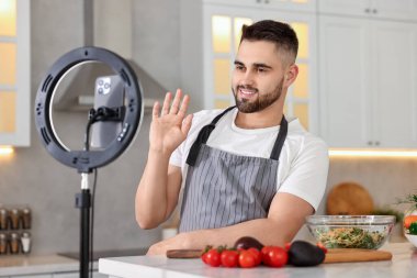 Yemek blogcusu mutfakta akıllı telefon ve yüzük lambasıyla video kaydederken yemek pişiriyor.