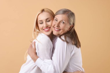 Family portrait of young woman and her mother on beige background