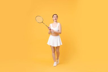 Turuncu arka planda badminton raketi olan genç bir kadın.