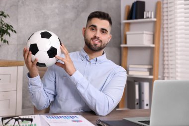 Masasında futbol topu olan genç bir adam.