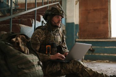 Military mission. Soldier in uniform using laptop inside abandoned building