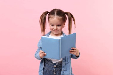 Pembe arka planda kitap okuyan sevimli küçük kız.