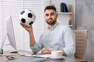 Masasında futbol topu olan genç bir adam.