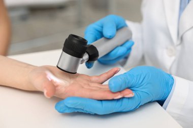 Dermatoskoplu bir dermatolog klinikteki beyaz masada hastayı muayene ediyor.