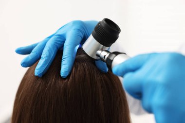 Dermatoskoplu trikoloğum klinikte hastanın saçını inceliyor.