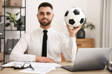 Masasında futbol topu olan genç bir adam.