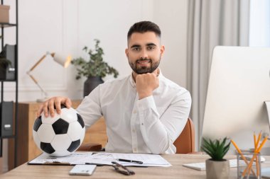 Masasında futbol topu olan genç bir adam.