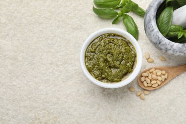 Lezzetli pesto sosu kasede, fesleğende, çam fıstığında ve açık gri masada kaşık, düz yerde. Metin için boşluk