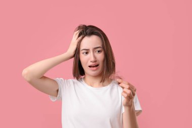 Duygusal kadın pembe arka planda bir tutam dökülmüş saçı tutuyor. Alopecia sorunu