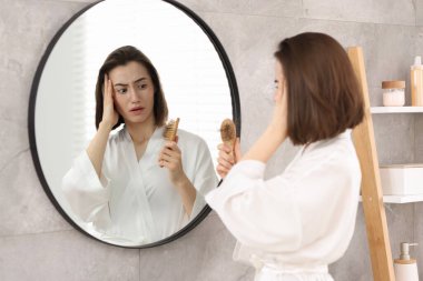 Stresli bir kadın evde aynanın yanında saçlarını tarıyor. Alopecia sorunu
