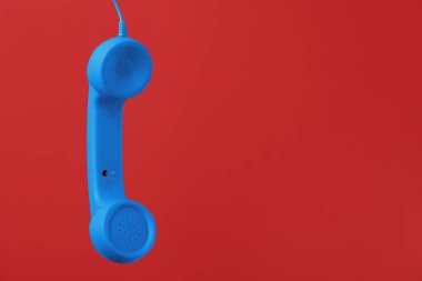 Kırmızı arka planda asılı mavi telefon. Metin için boşluk