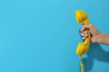 Açık mavi arka planda sarı telefon taşıyan kadın, yakın plan. Metin için boşluk