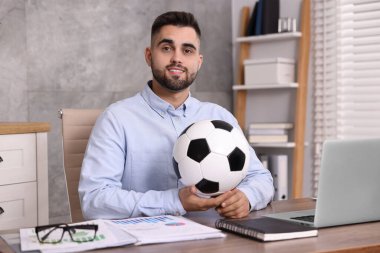 Masasında futbol topu olan genç bir adam.