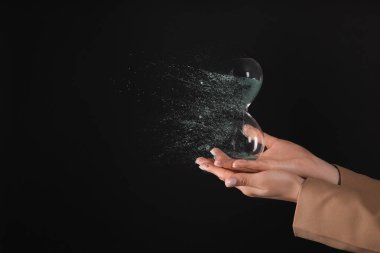 İş kadını elinde siyah arka planda çözünen kum saati tutuyor, yakın plan. Zaman tükeniyor.
