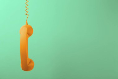 Açık yeşil arka planda asılı turuncu telefon ahizesi. Metin için boşluk