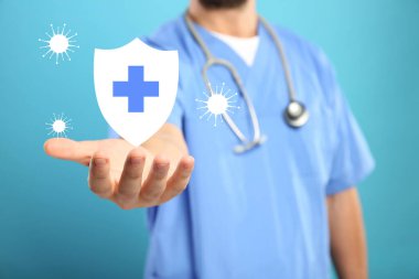 Bağışıklık sistemi virüsleri engelliyor. Doktor açık mavi arkaplanda kalkanın resmini tutuyor, yakın plan.