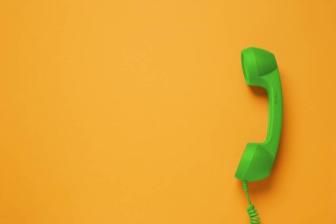 Yeşil telefon ahizesi turuncu arka planda, üst manzara. Metin için boşluk