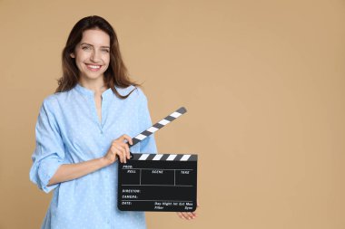 Making movie. Smiling woman with clapperboard on beige background. Space for text clipart