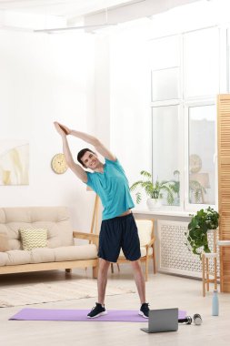 Çevrimiçi fitness eğitmeni. Evde dizüstü bilgisayar başında egzersiz yapan bir adam.