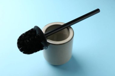 Açık mavi arkaplanda tuvalet fırçası ve tutucu