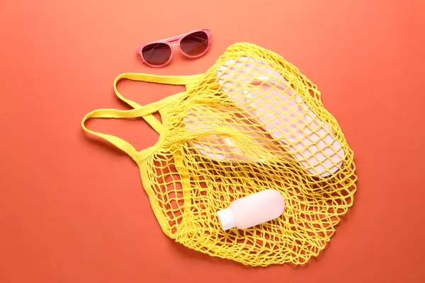 stock image String bag, sunglasses, cosmetic product and slippers on coral background, top view