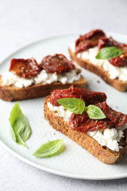 Lezzetli ricotta bruschettalar, güneşte kurutulmuş domates ve fesleğen, yakın plan.