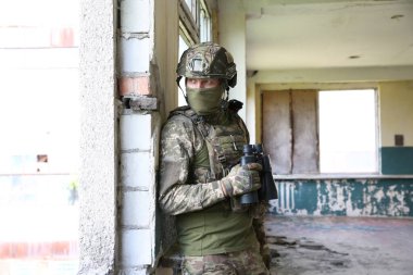 Military mission. Soldier in uniform with binoculars inside abandoned building
