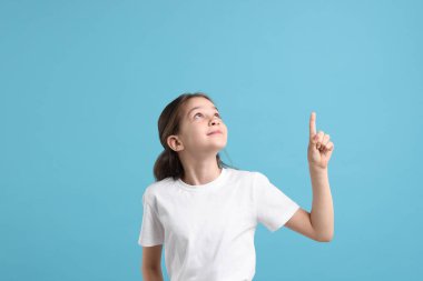 Güzel kız açık mavi arka plandaki bir şeyi işaret ediyor.