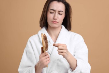 Üzgün kadın saçlarını açık kahverengi arka planda fırçadan alıyor. Alopecia sorunu
