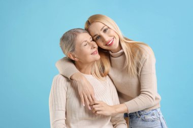 Family portrait of young woman and her mother on light blue background