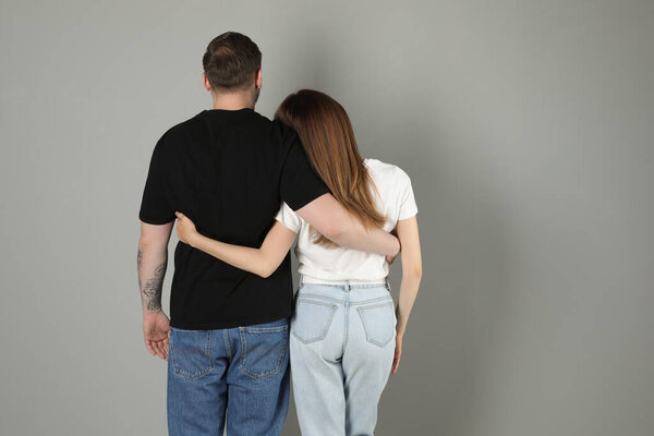 Cute couple hugging on grey background, back view. Space for text