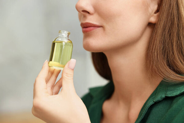 Aromatherapy. Woman with bottle of essential oil on light background, closeup