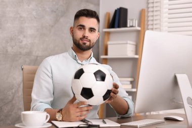 Masasında futbol topu olan genç bir adam.