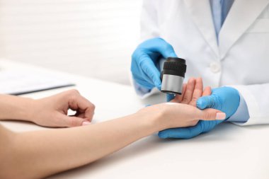 Dermatoskoplu bir dermatolog klinikteki beyaz masada hastayı muayene ediyor.