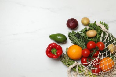 Vejetaryen yemek servisi. Farklı taze sebzelerle dolu ağ torbası ve beyaz mermer arka planda meyveler, düz. Metin için boşluk