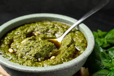 Lezzetli pesto sosu kasede, kaşık ve fesleğen masada, yakın plan.