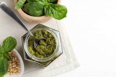 Kavanozda pesto sosu, kaşık, çam fıstığı ve fesleğen, beyaz masa, üst manzara. Metin için boşluk