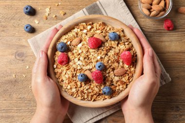 Ahşap masada meyveli ve fındıklı bir kase lezzetli granola taşıyan kadın.