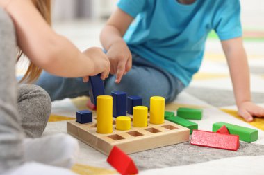 Küçük çocuklar, halıdaki ahşap geometrik figürlerle oynuyor, yakın plan. Motor beceriler geliştirmek için anaokulu aktiviteleri