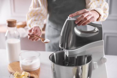 Kadın, kapalı mekânda hamur toplarken tezgah karıştırıcısına şeker ekliyor.