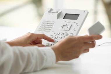 Assistant dialing number on telephone against blurred background, closeup