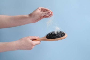 Woman taking her lost hair from brush on light blue background, closeup