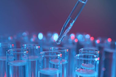 Renk arka planında pipetten test tüpüne sıvı damlatılıyor, yakın plan