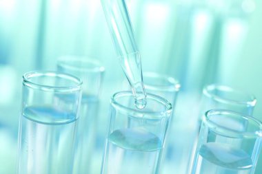 Turkuaz arka planda pipetten test tüpüne sıvı damlatılıyor.