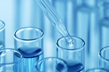 Işık arka planında pipetten test tüpüne sıvı damlatılıyor, yakın plan