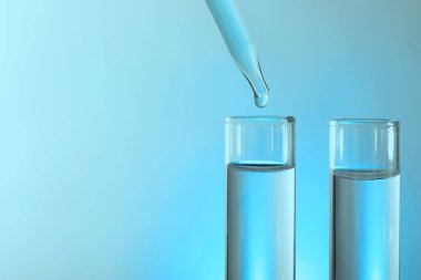 Işık arka planında pipetten test tüpüne sıvı damlatılıyor, yakın plan. Metin için boşluk